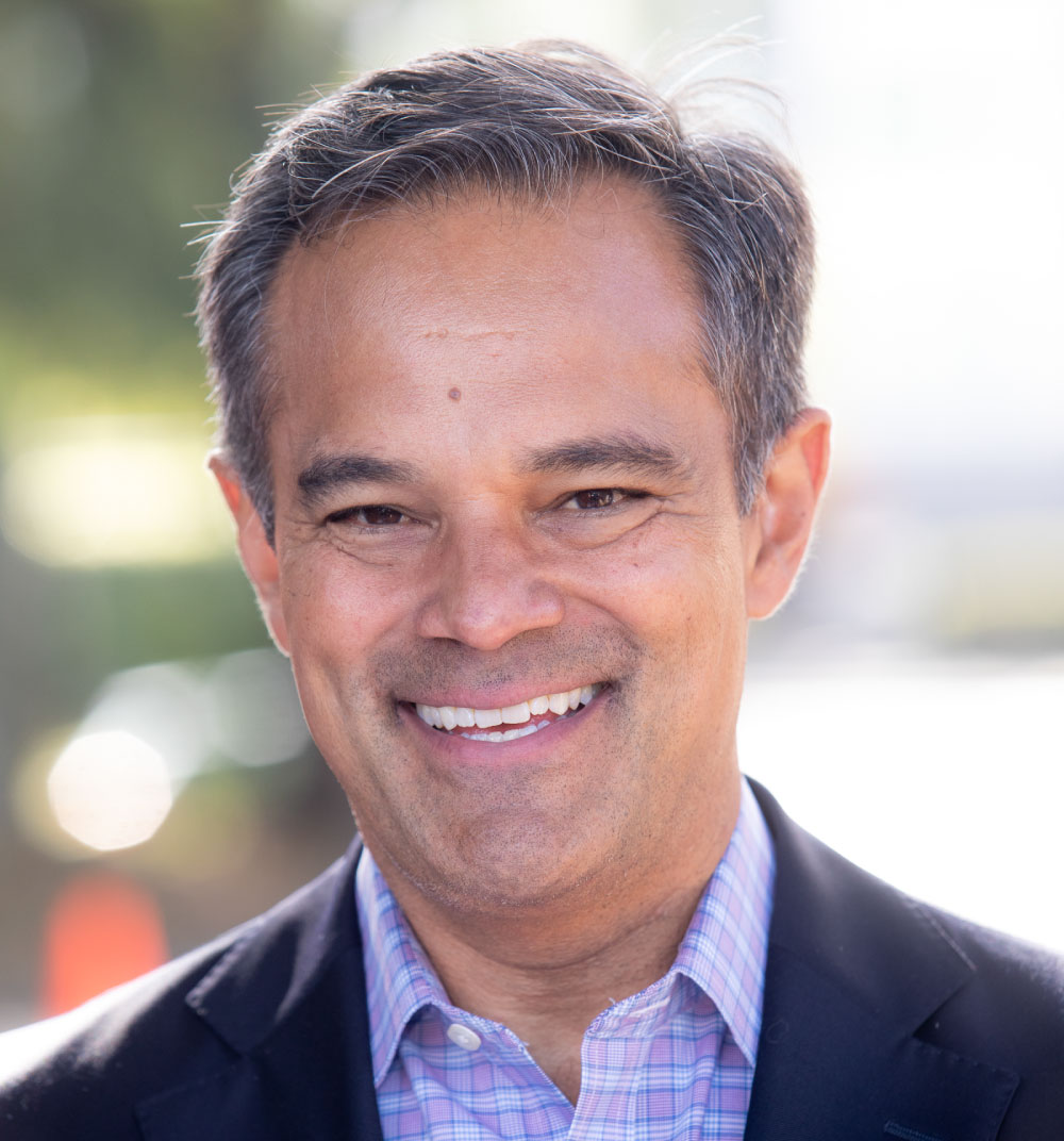 A man in a suit and tie smiles warmly at the camera, exuding confidence and professionalism.