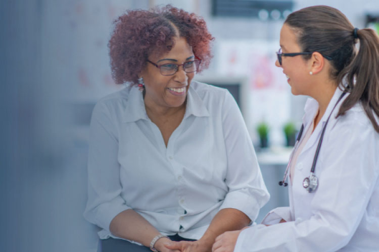 Doctor talking with a patient, both smiling and seated together in a clinical setting.