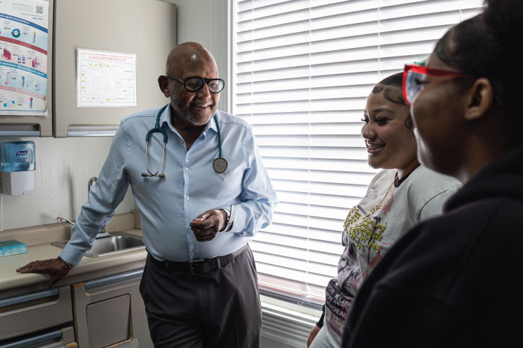 Doctor speaking with two patients in an exam room, smiling during a healthcare consultation.